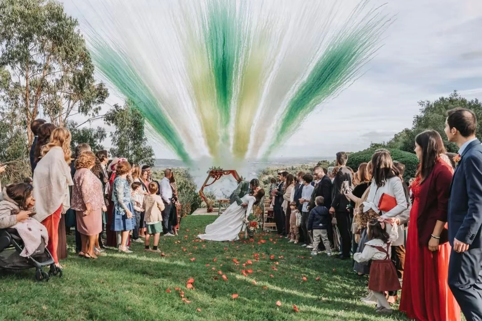 Noivos celebram o casamento com os convidados, entre árvores e fumos verdes e brancos